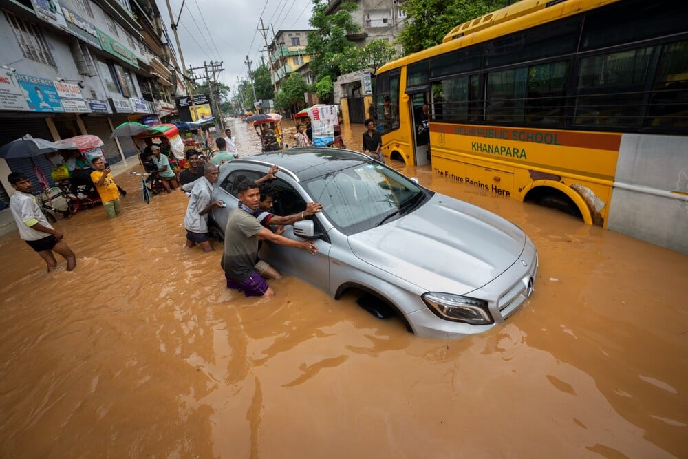 Gauhátí – Na snímku se lidé snaží tlačit auto uvízlé na zaplavené cestě po silných deštích v Gauhátí v indickém státě Ásám v úterý 14. června 2022.