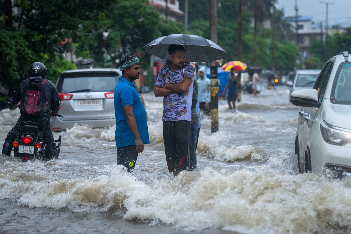 Guváhátí – Muži stojí na zaplavené ulici po prudkém dešti ve městě Guváhátí v indickém státě Ásám. 16. června 2022.