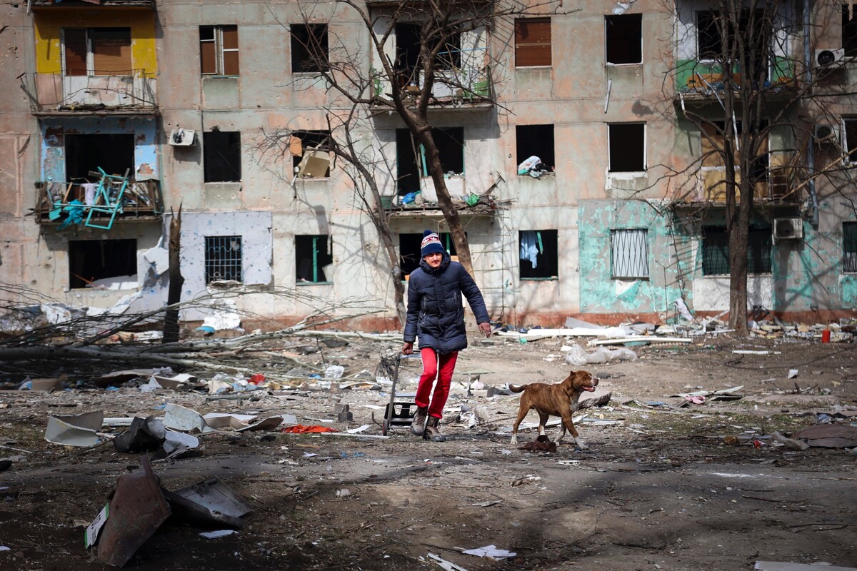 Muž kráča so psom okolo bytovky zničenej po ostreľovaní na okraji ukrajinského Mariupola na území pod kontrolou separatistickej vlády Doneckej ľudovej republiky. (29. marca 2022)