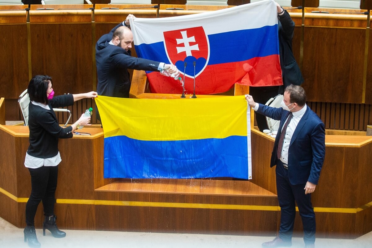 Andrej Medvecký, Peter Krupa (obidvaja ĽSNS) držia slovenskú vlajku a dole zľava Jana Bittó Cigániková a Miroslav Žiak (obidvaja SaS) držia ukrajinskú vlajku počas rokovania parlamentu v Bratislave 8. februára 2022.