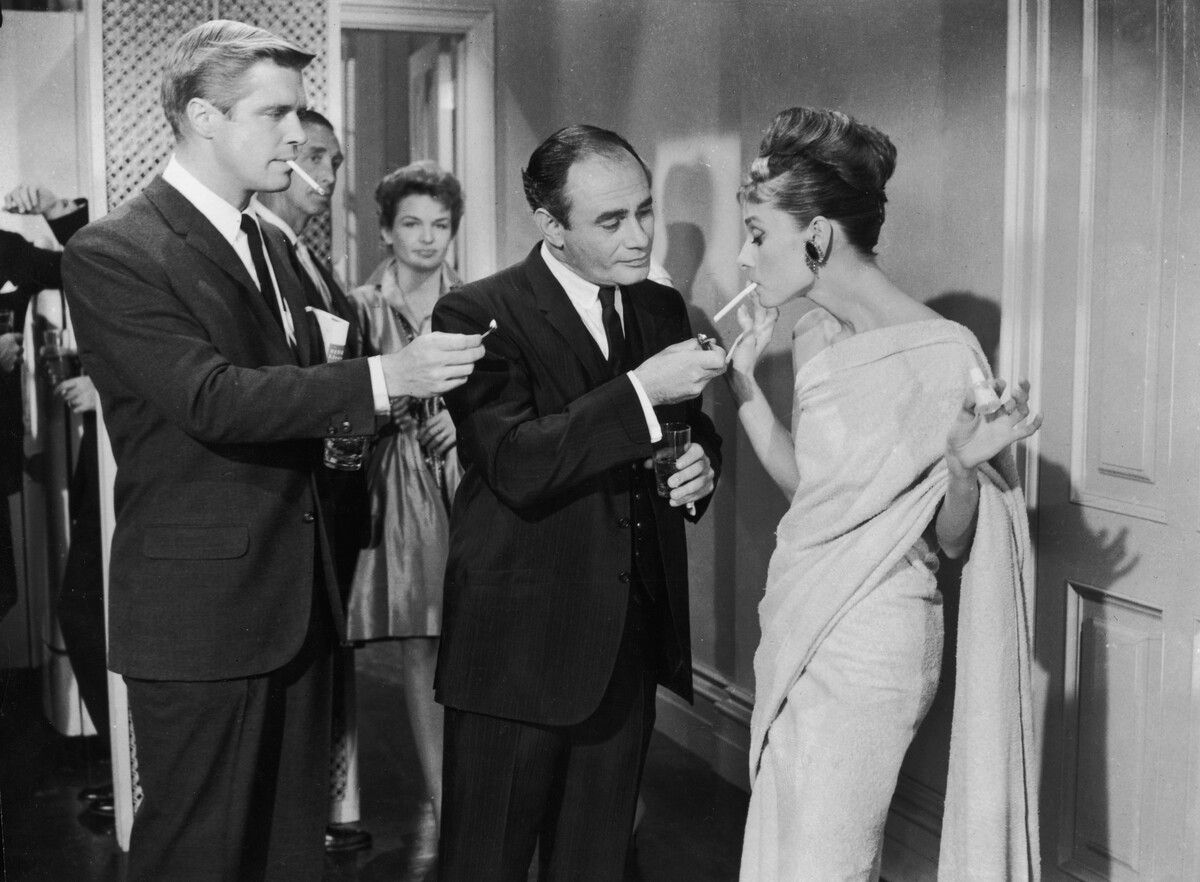 George Peppard a Martin Balsam soutěží o zapálení cigarety Audrey Hepburn na formálním večírku ve snímku režiséra Blakea Edwardse „Snídaně u Tiffanyho“.