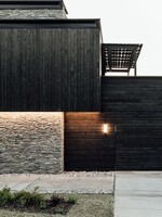 Černý dřevěný obklad v kombinaci s kamenem na fasádě jako kontrast k modernímu interiéru, který obývá mladá rodina
