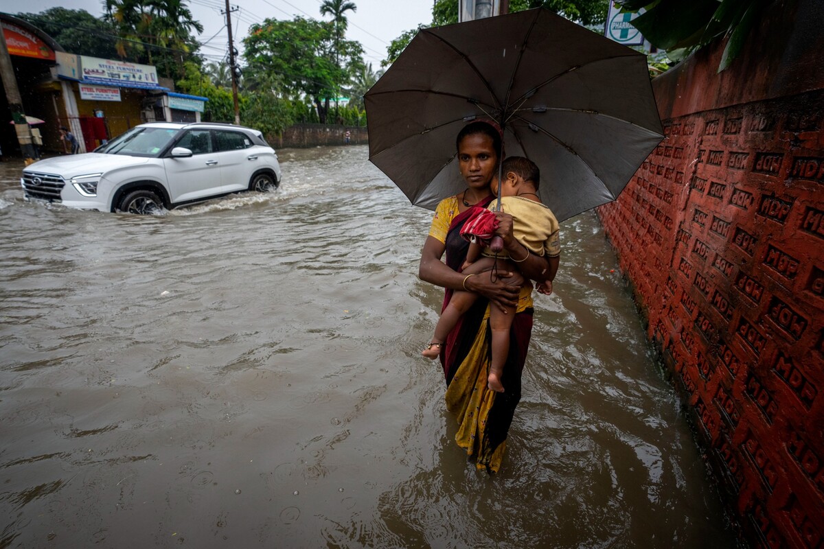 Guváhátí – Žena s dítětem v náručí se brodí zaplavenou ulicí po prudkém dešti ve městě Guváhátí v indickém státě Ásám. 16. června 2022.