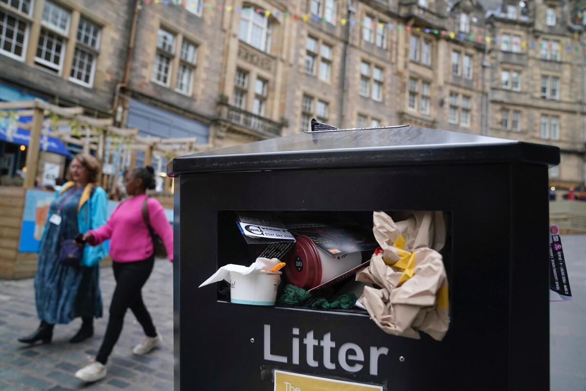 Ľudia kráčajú okolo preplnených smetných košov na ulici v Edinburghu. Edinburghskí smetiari totiž vyhlásili 12-dňový štrajk, kvôli čomu sú v meste preplnené koše a nemá ich kto vyprázdniť. Odbory totiž odmietli ich návrh na zvýšenie miezd o 3,5 percenta. (20. augusta 2022)
