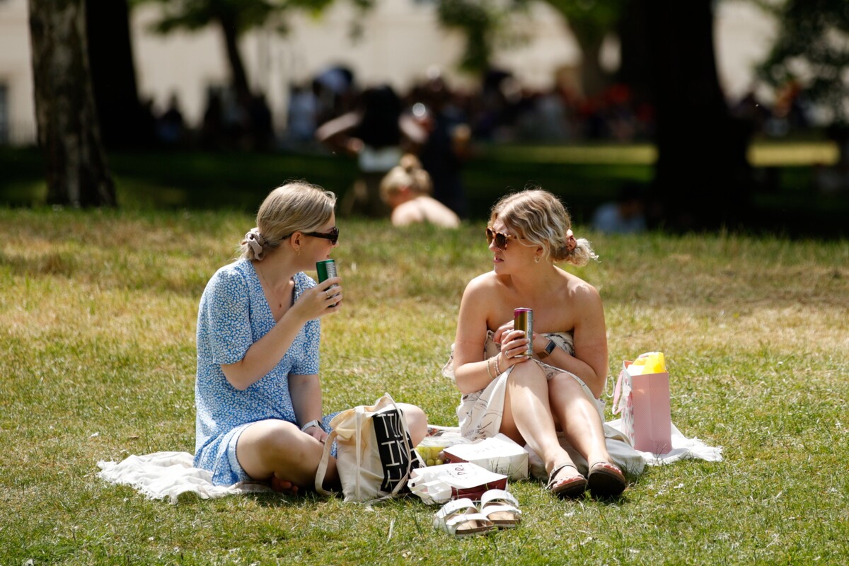 Dve ženy sedia na tráve na pikniku v St. James's Parku v Londýne 16. júna 2022 v teplom počasí.