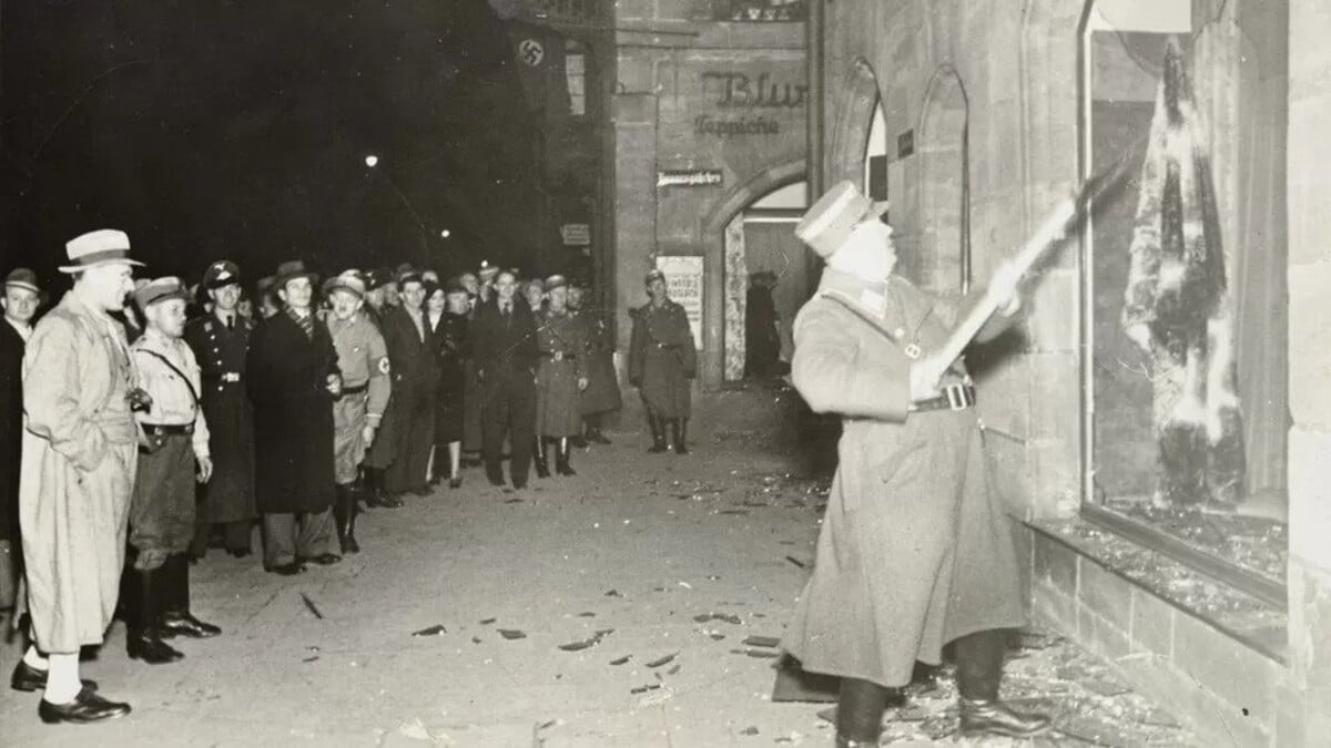 Na ničenie židovského majetku sa prizerali aj občania. Niektorým na tvárach pohráva letmý úsmev.