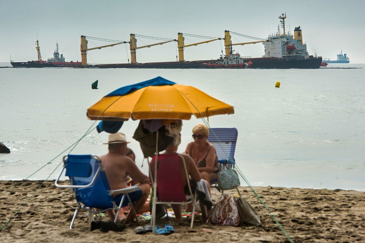 Skupina ľudí sedí na pláži pred nákladnou loďou OS 35, ktorá leží na morskom dne pri pobreží Gibraltáru. Úrady uviedli, že podnikli všetky kroky k tomu, aby sa loď celkom nepotopila po svojej kolízii s tankerom prepravujúcim skvapalnený zemný plyn. (30. august 2022)