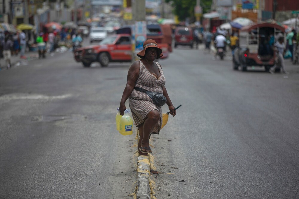 Žena predáva pohonné hmoty v plastových fľašiach na ulici v Port-au-Prince na Haiti. Haitskí demonštranti vo štvrtok pálili pneumatiky a blokovali ulice hlavného mesta na protest proti nedostatku pohonných hmôt. Urobili tak napriek tomu, že haitský hlavný palivový terminál opätovne obnovil dodávky, ktoré boli pozastavené pre prebiehajúcu vojnu gangov. (14. júla 2022)